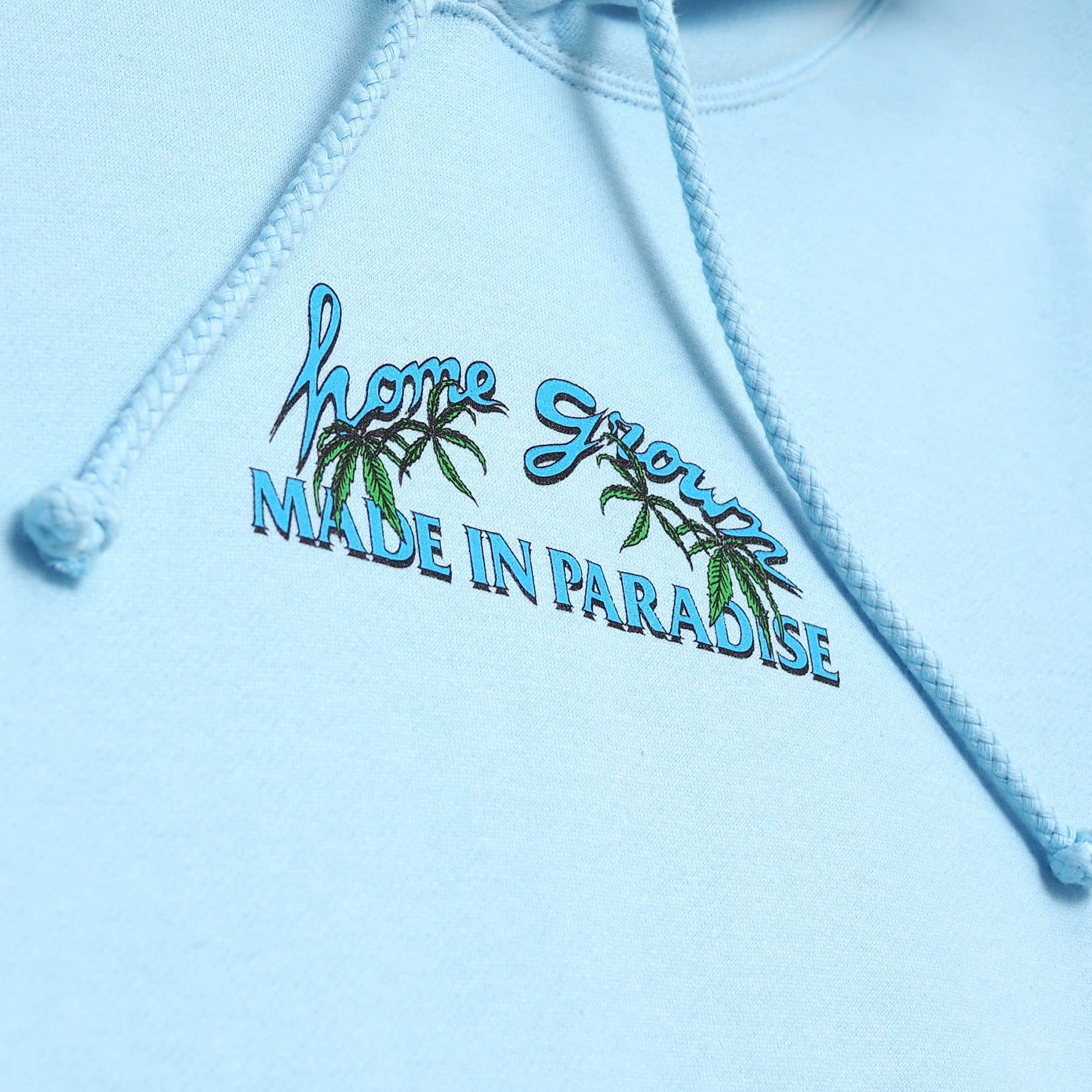 Close-up view of front graphic print of Made in Paradise Homegrown Collection "HOME GROWN" light blue hoodie